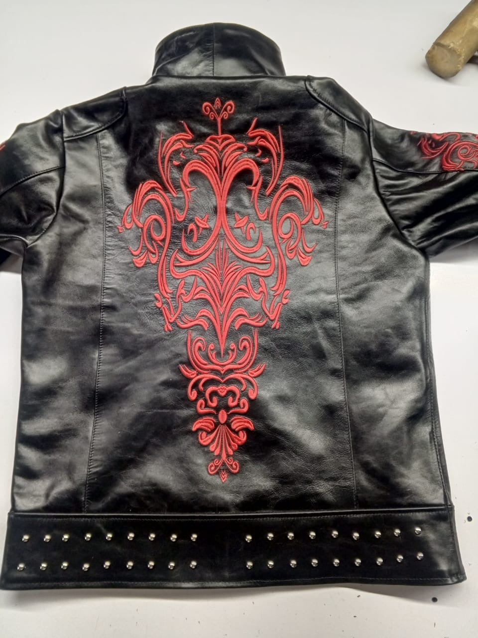 Back of black leather jacket with large red ornamental embroidery and studded hem