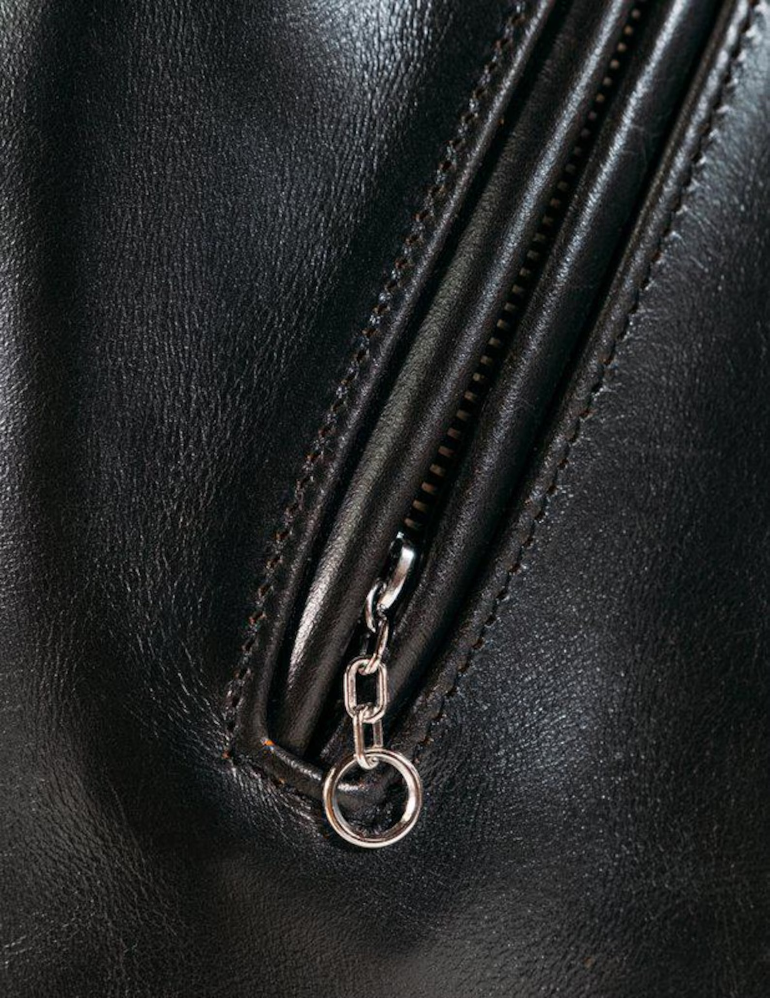 Close-up of a black leather bag with a zipper and keychain detail.