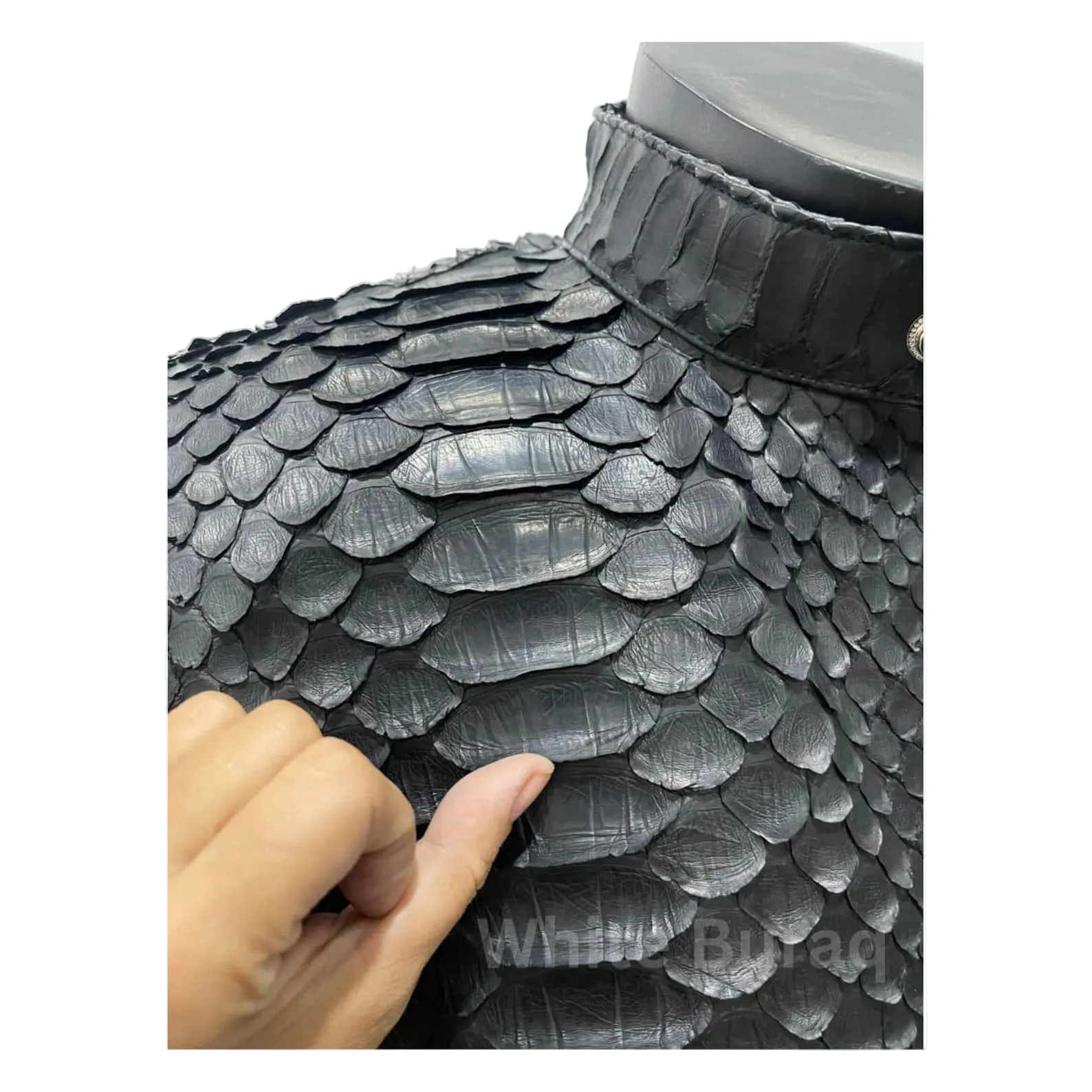 Close-up of a black dragon scale-patterned helmet with a hand touching it