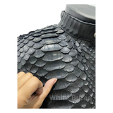 Close-up of a black dragon scale-patterned helmet with a hand touching it