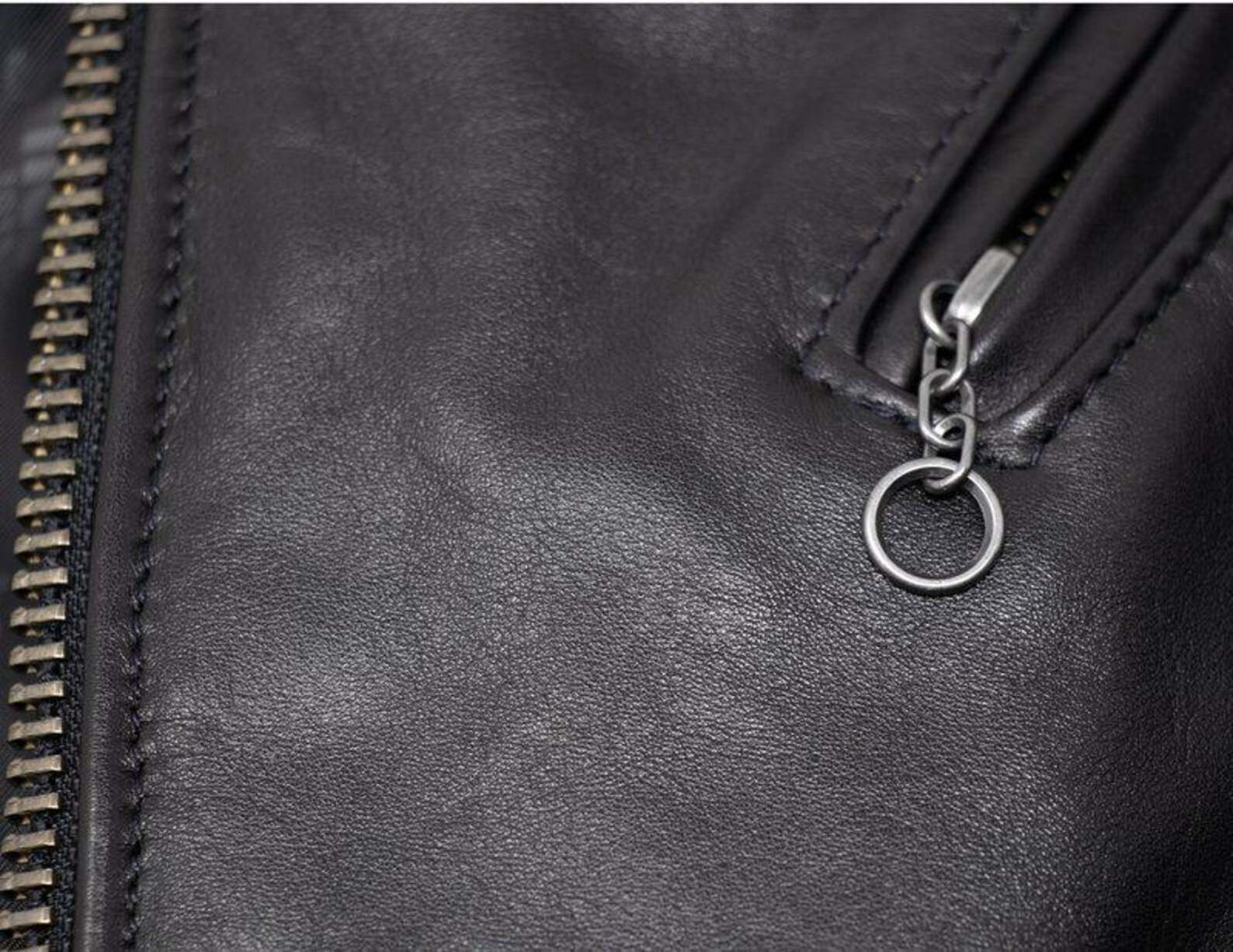 Close-up of a black leather jacket with a zipper and keychain detail.