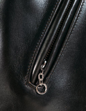 Close-up of a black leather bag with a zipper and keychain detail.
