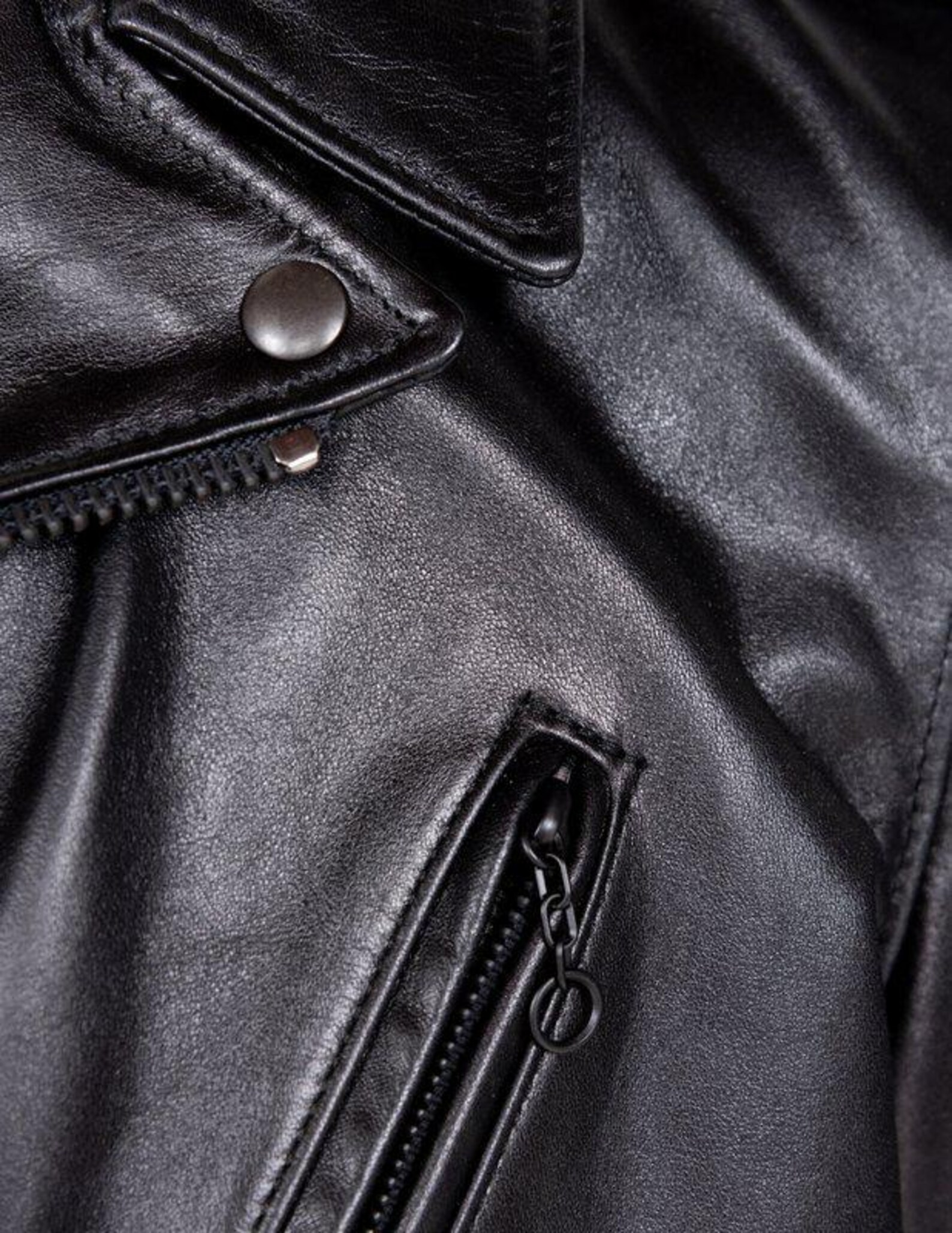 Close-up of a black leather jacket with zipper and button details.