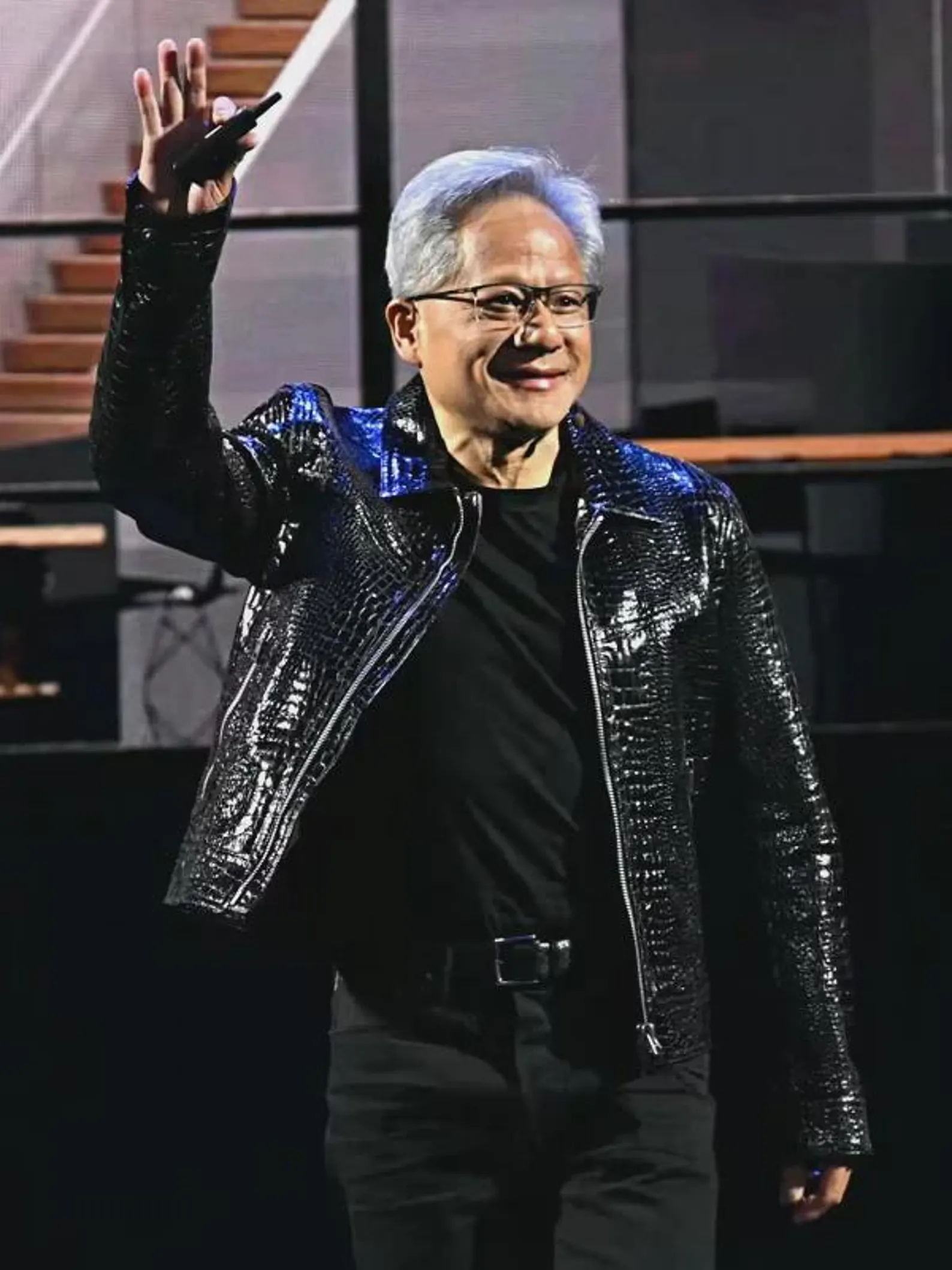 Man in a shiny black jacket waving on a stage
