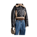 Person wearing a black leather jacket with shearling collar and blue jeans, holding a handbag.